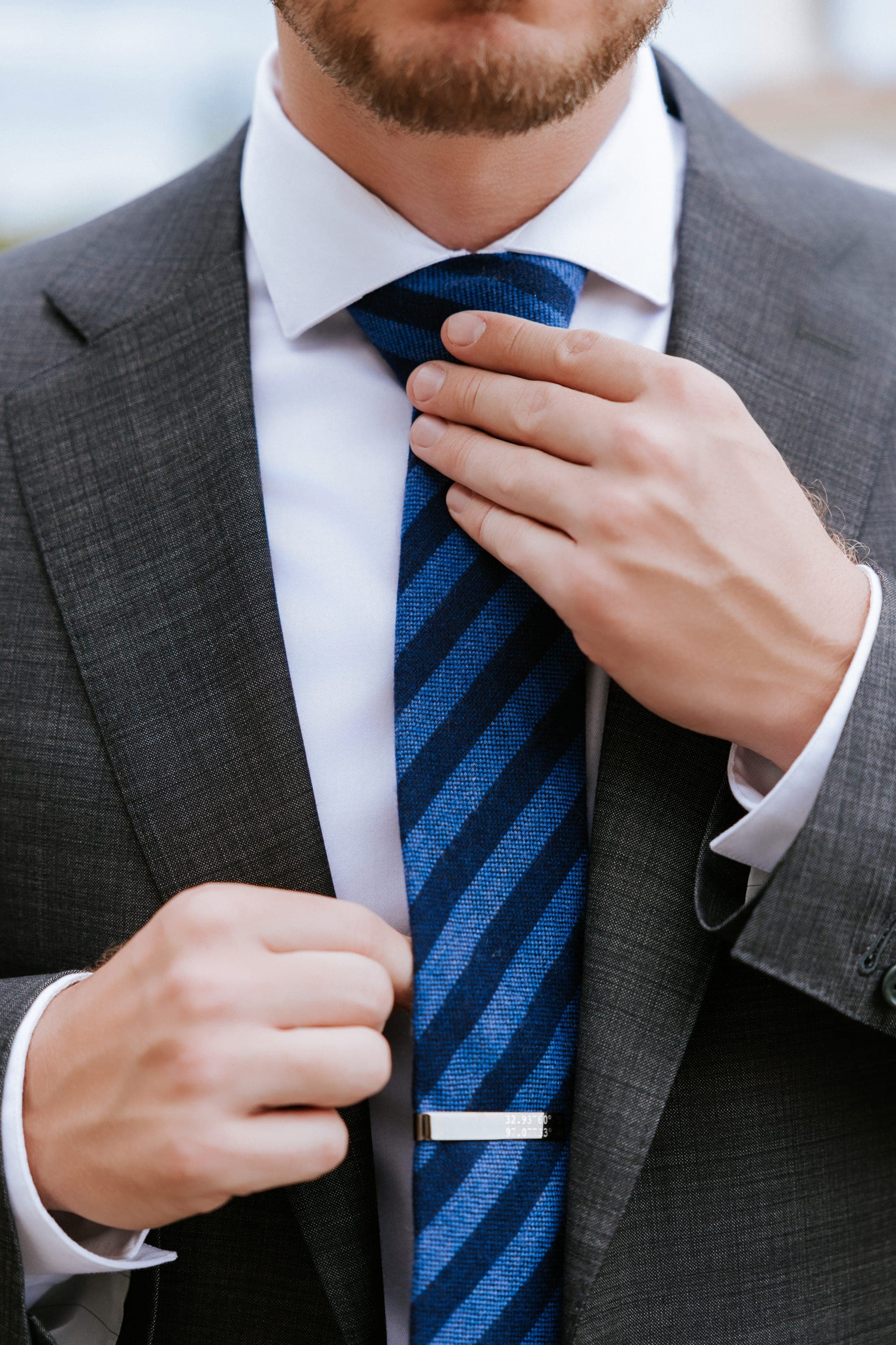 Eric straightening his navy striped tie and silver tie bar