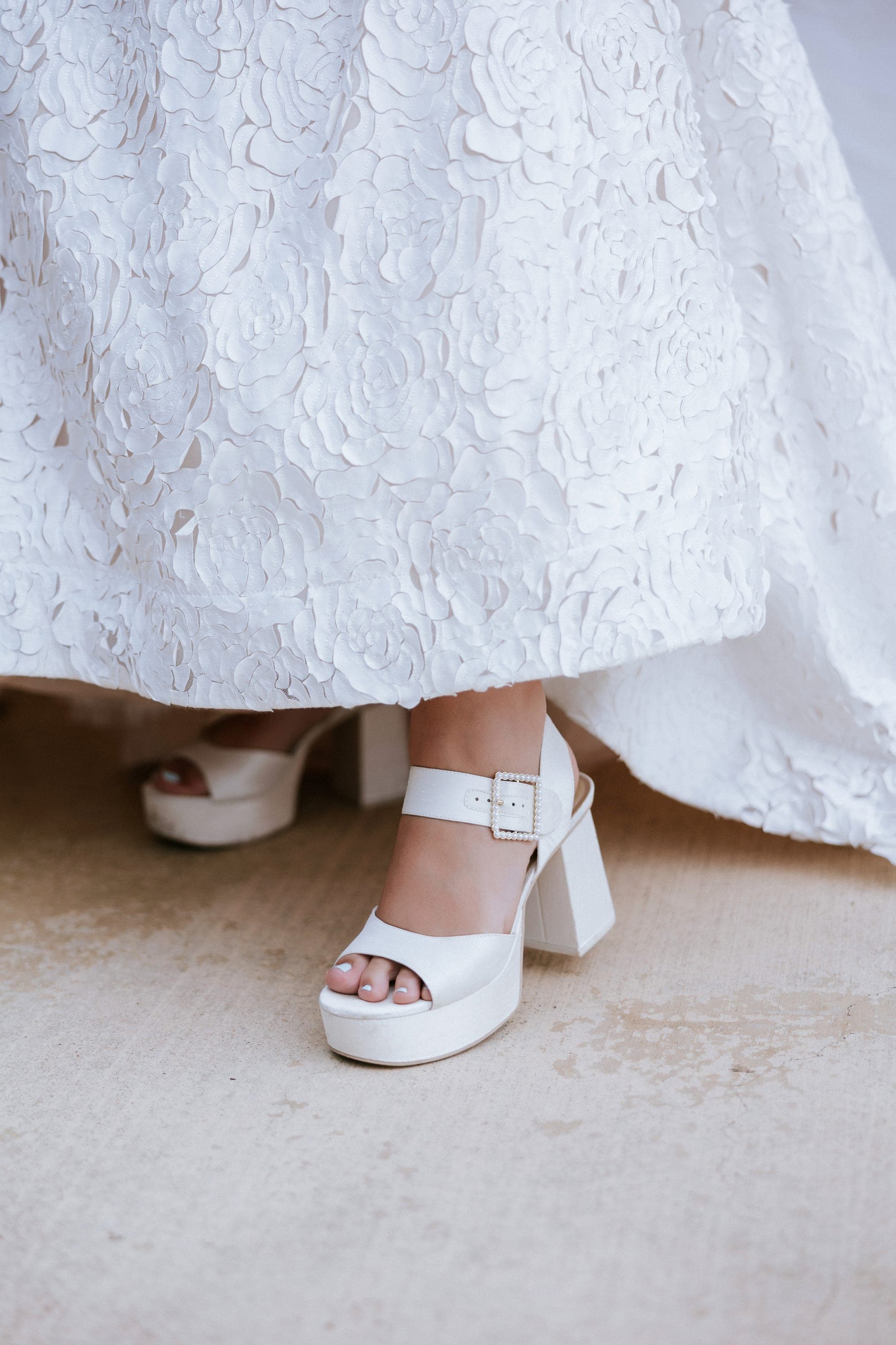 The sculpted lace hem of the gown over white platform heels