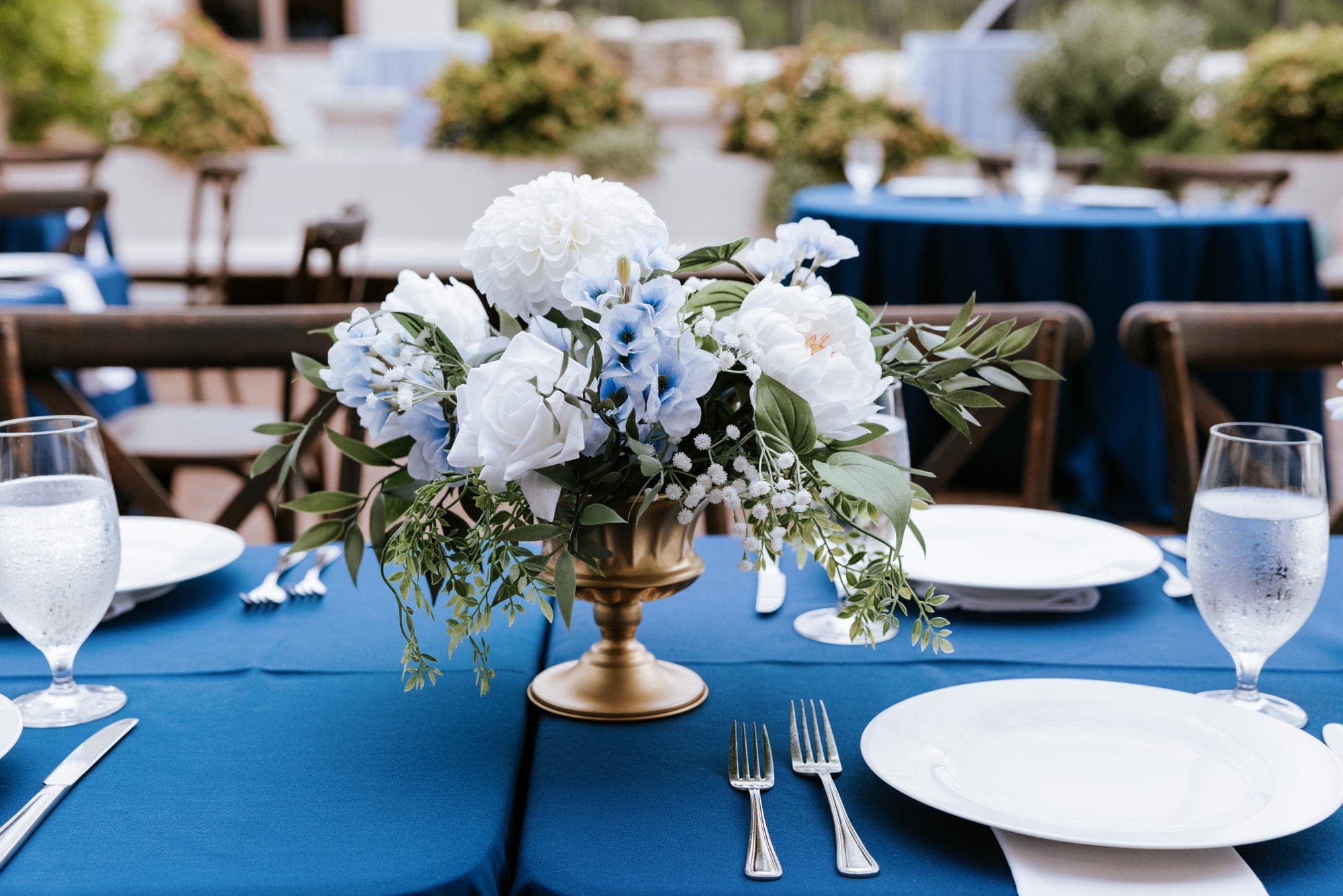 A gold compote centerpiece of white peonies and blue blooms on navy linen