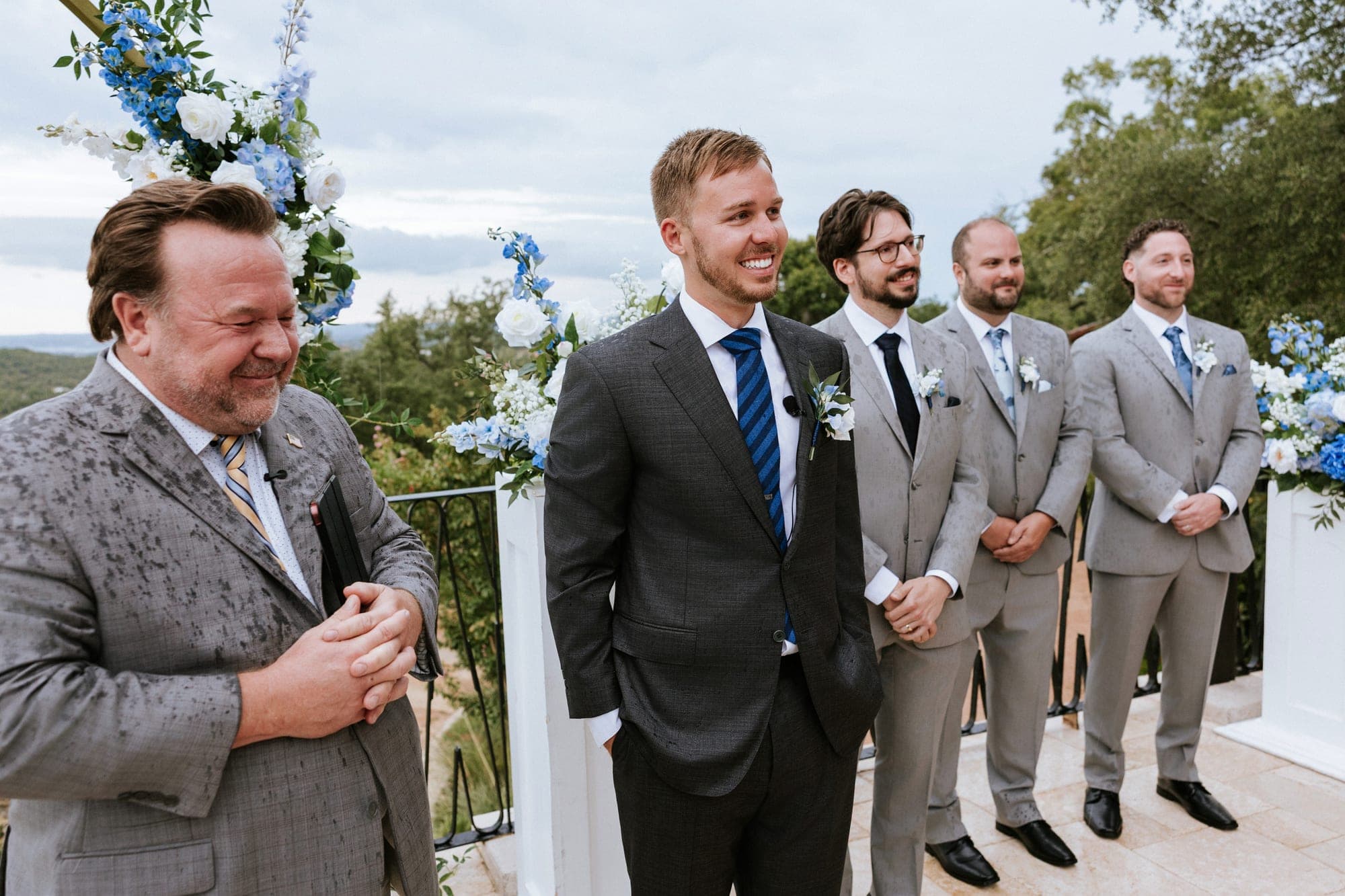 Eric laughing with the officiant and his groomsmen beneath the arch before the vows