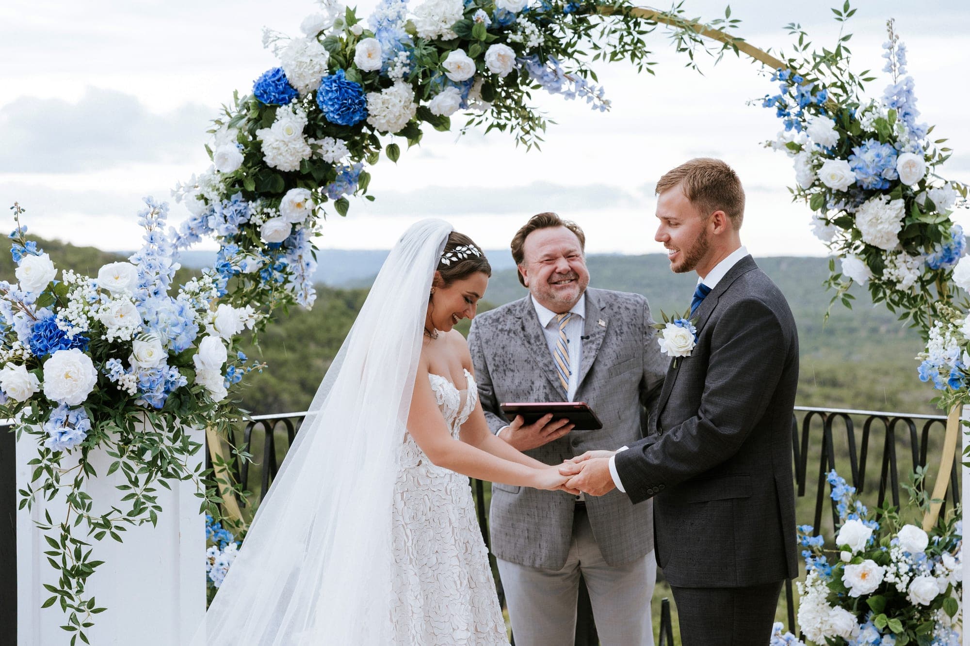 Kelsey and Eric holding hands through the vows at the floral arch