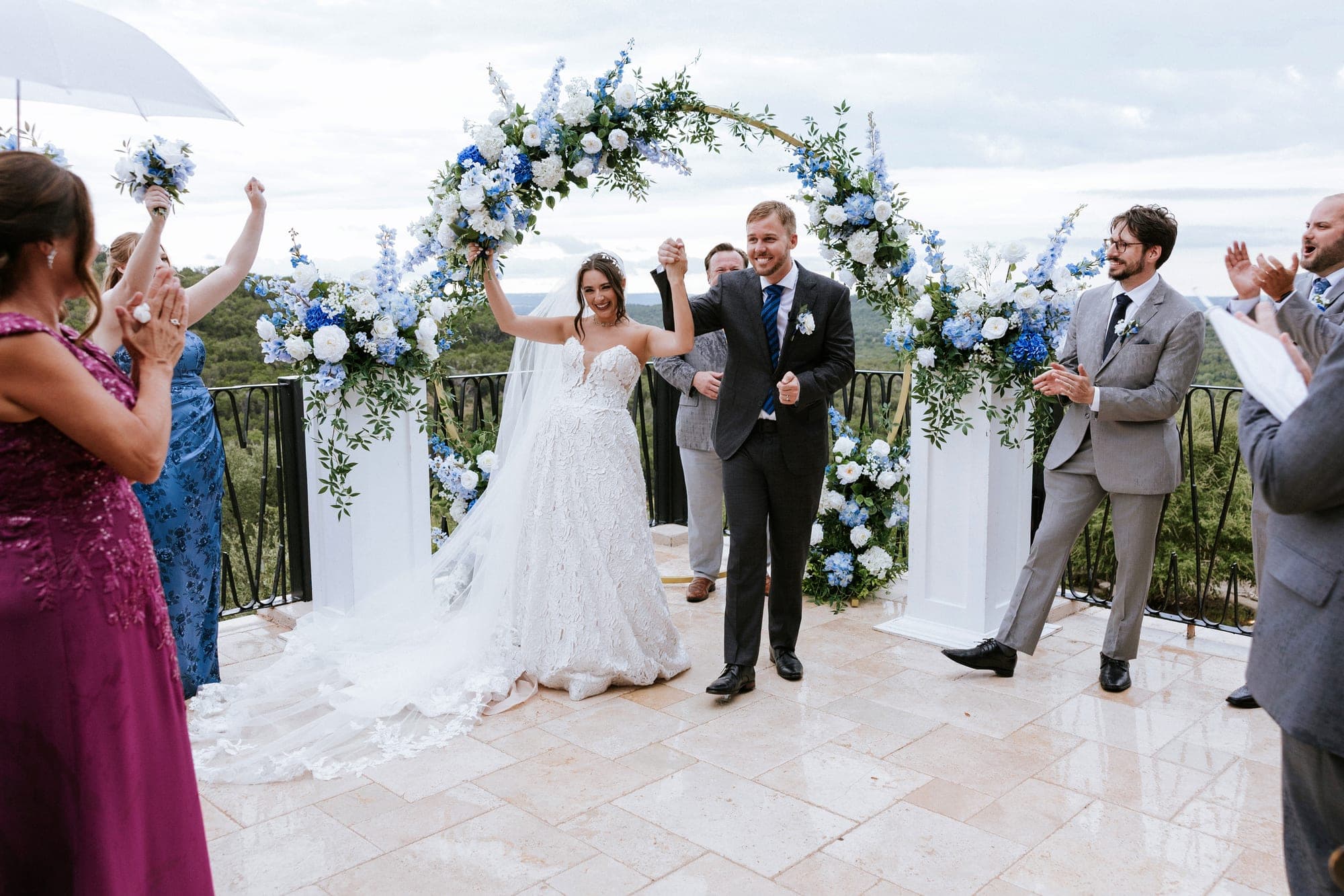 Just married, arms in the air beneath the arch as guests cheer