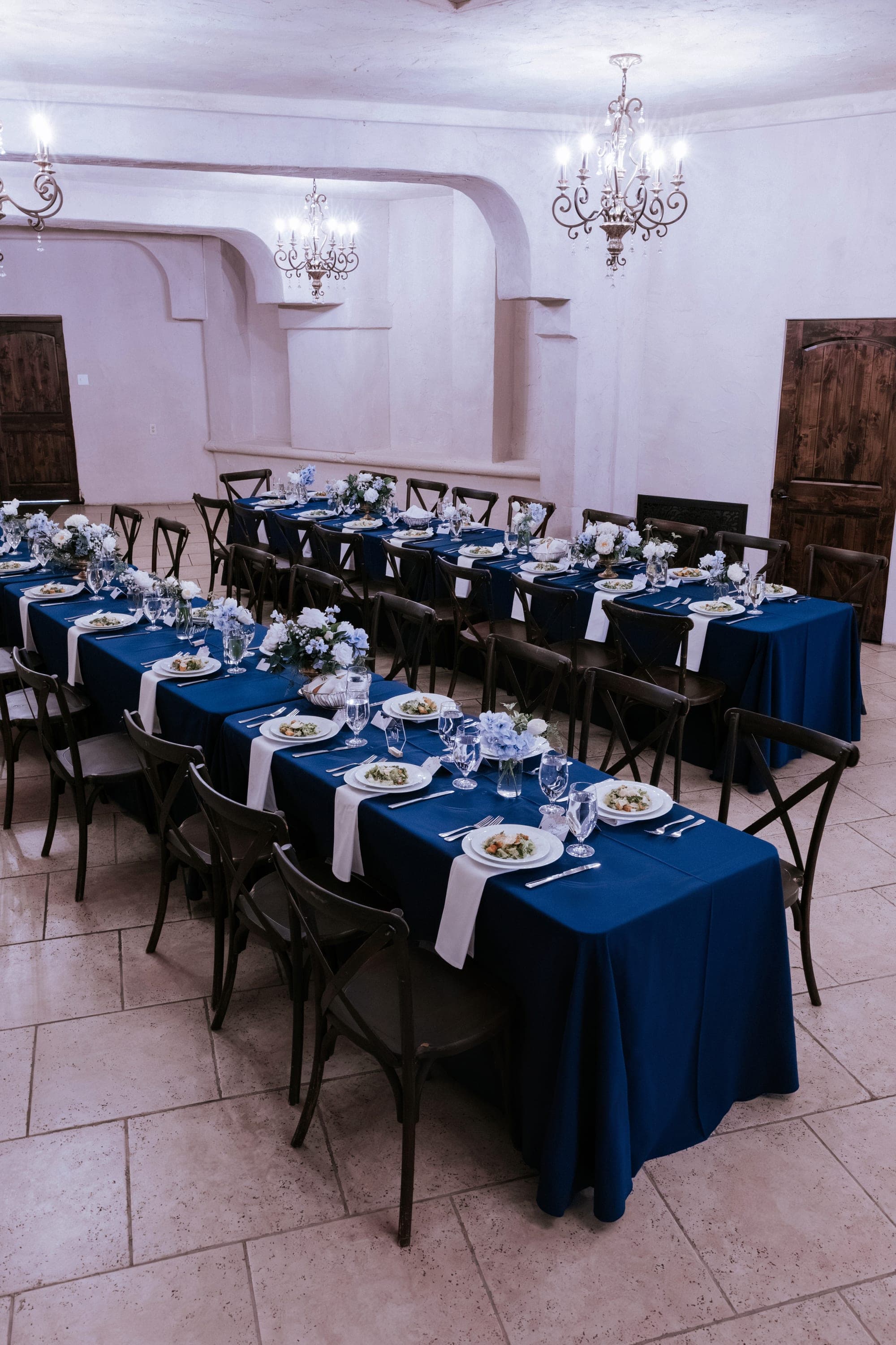 The villa dining room set with long navy tables beneath chandeliers
