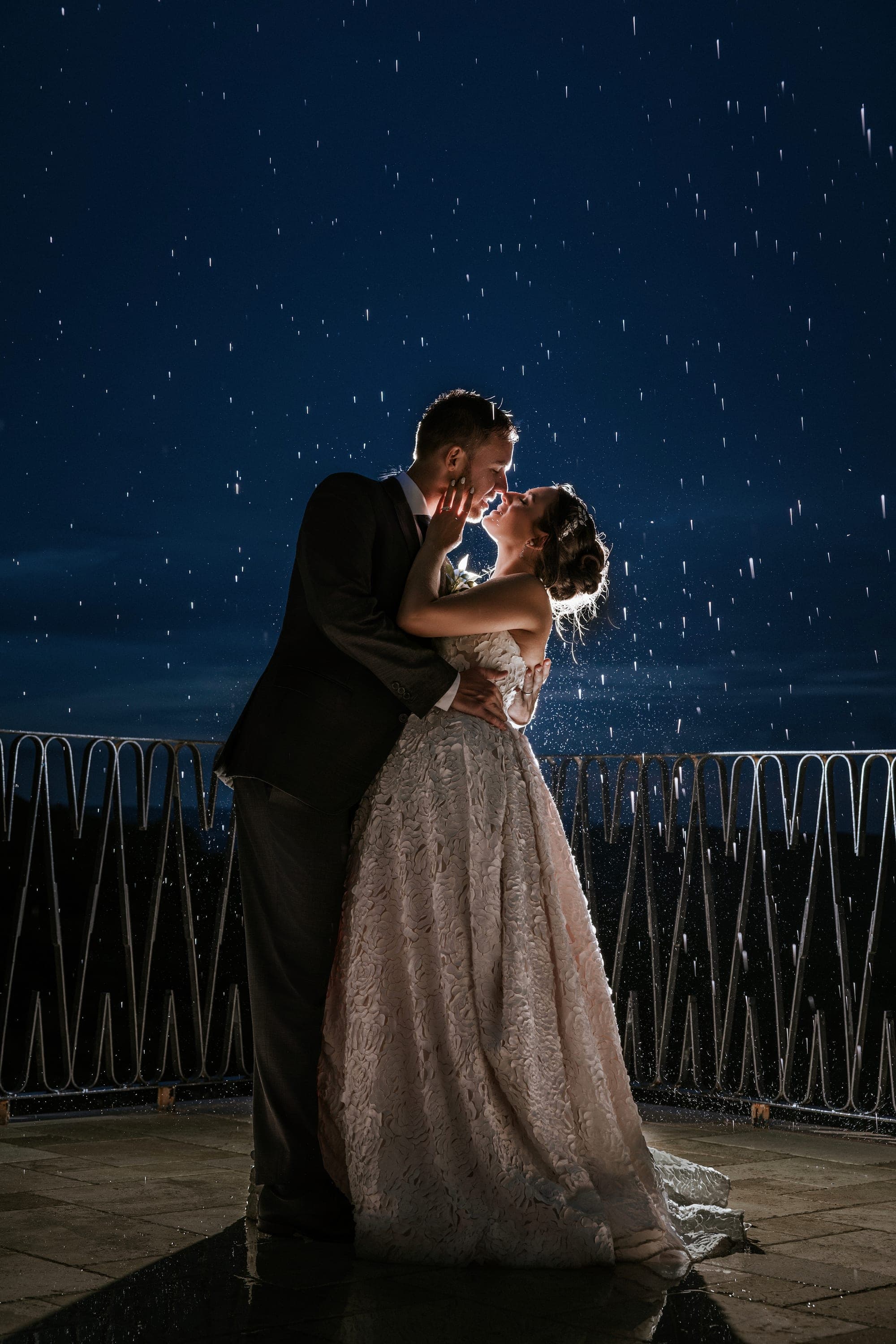 Kelsey and Eric kissing at night in backlit rain on the villa terrace