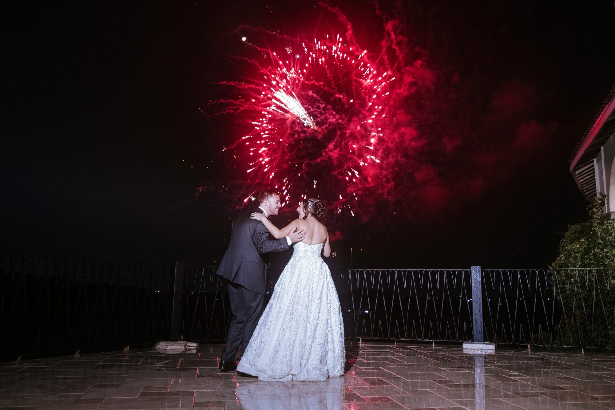 Red fireworks bursting over Kelsey and Eric on the rain-slicked terrace