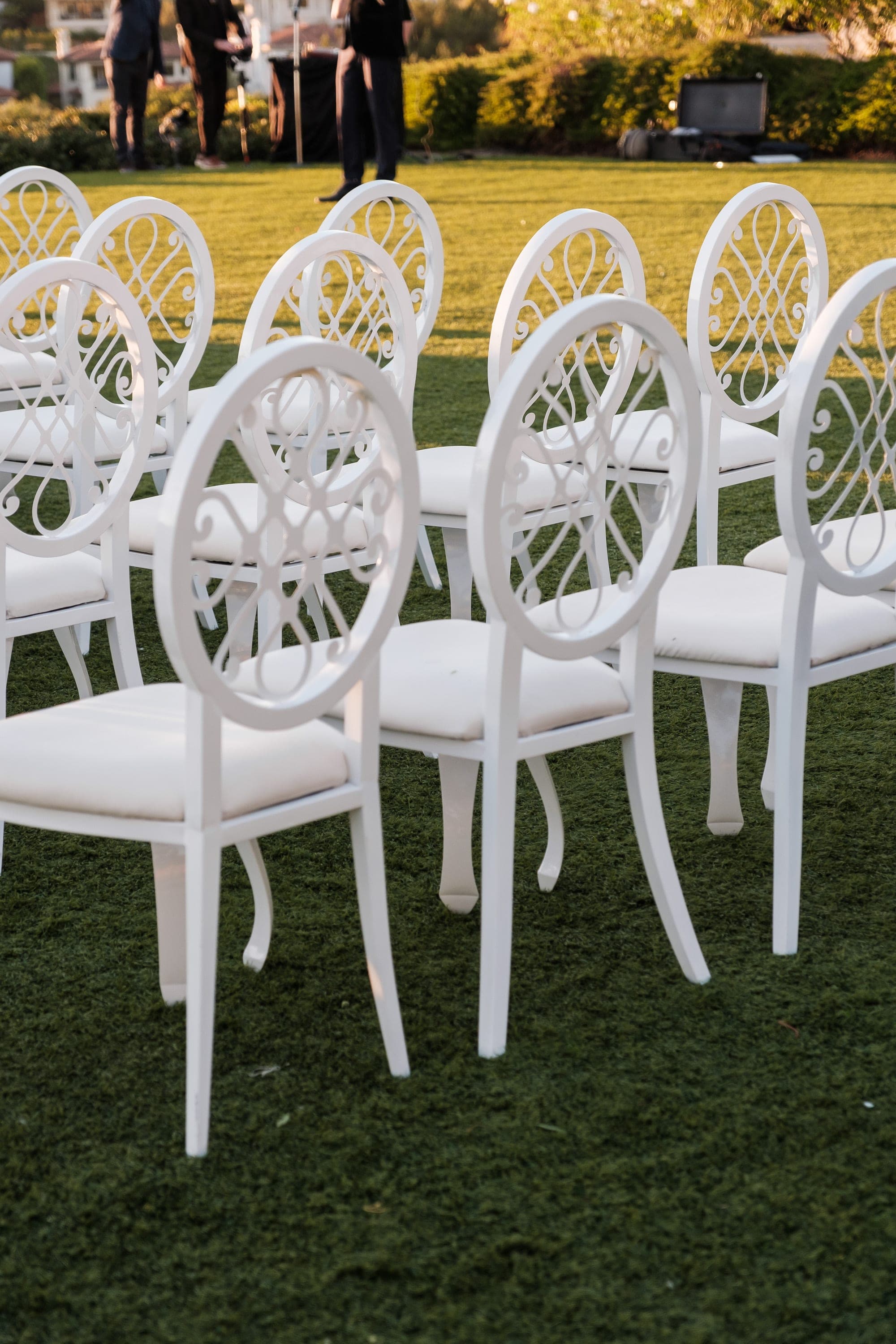 Rows of white oval-backed chairs on green grass with crew members standing in the background.