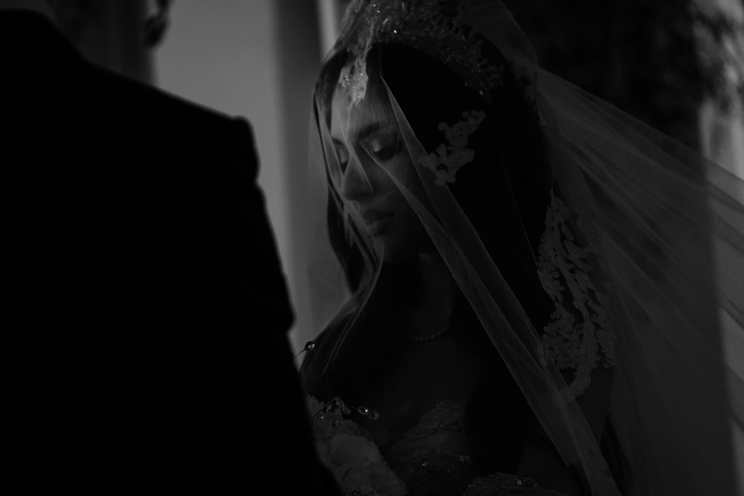 Black and white profile of a bride with downcast eyes wearing a beaded lace veil