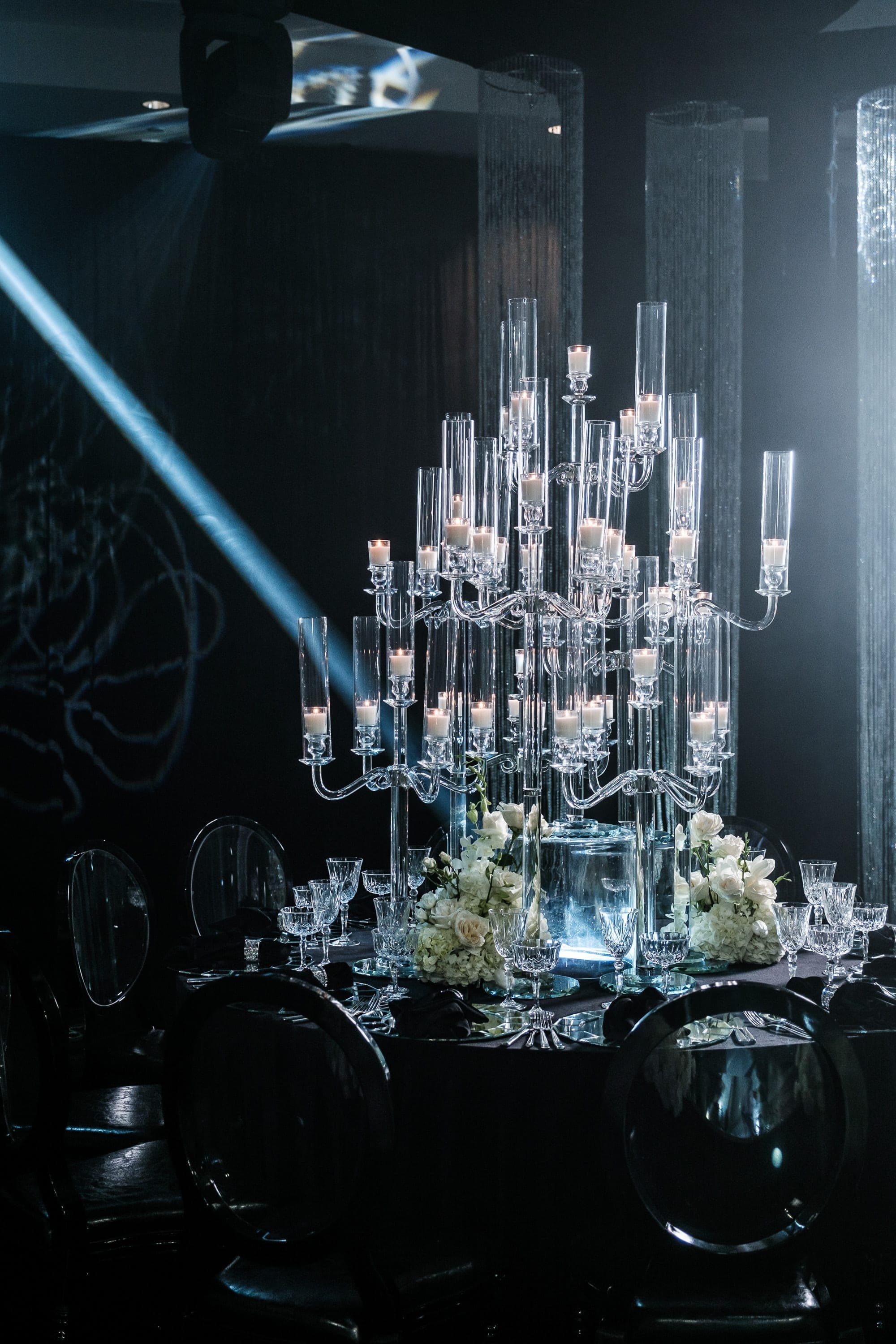 Tall crystal candelabra holding lit candles above a black table set with white roses and glassware.