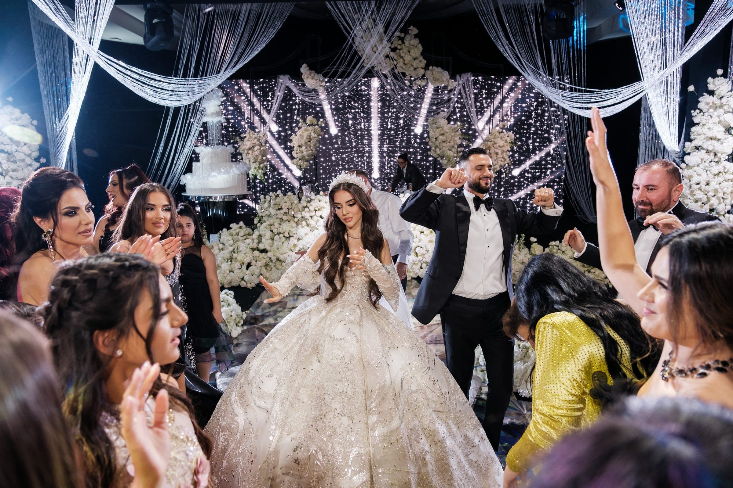 Bride and groom dance together as cheering guests raise their hands around the flower-filled dance floor.