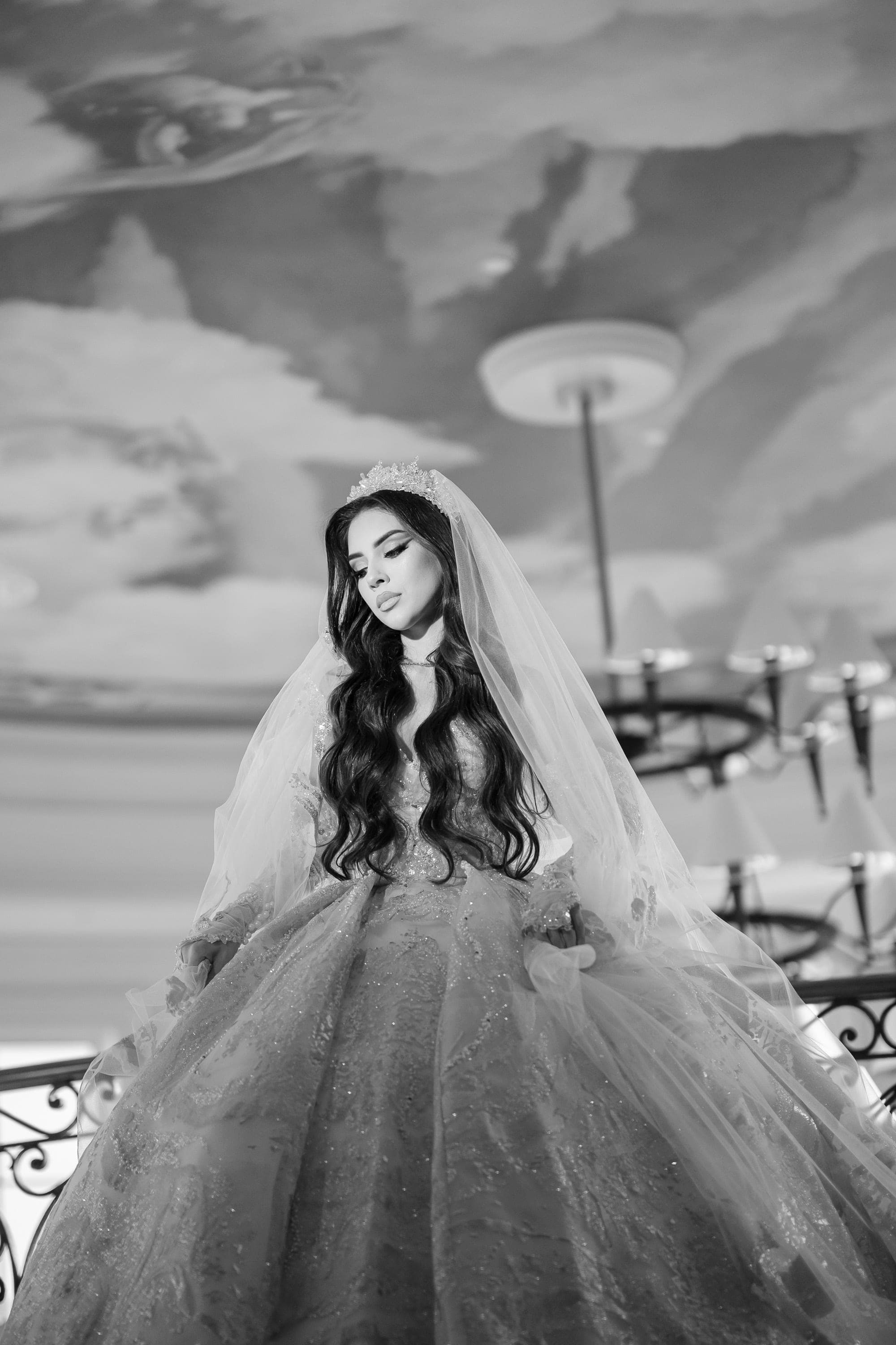 Black and white image of bride in full gown standing beneath a painted cloud ceiling.
