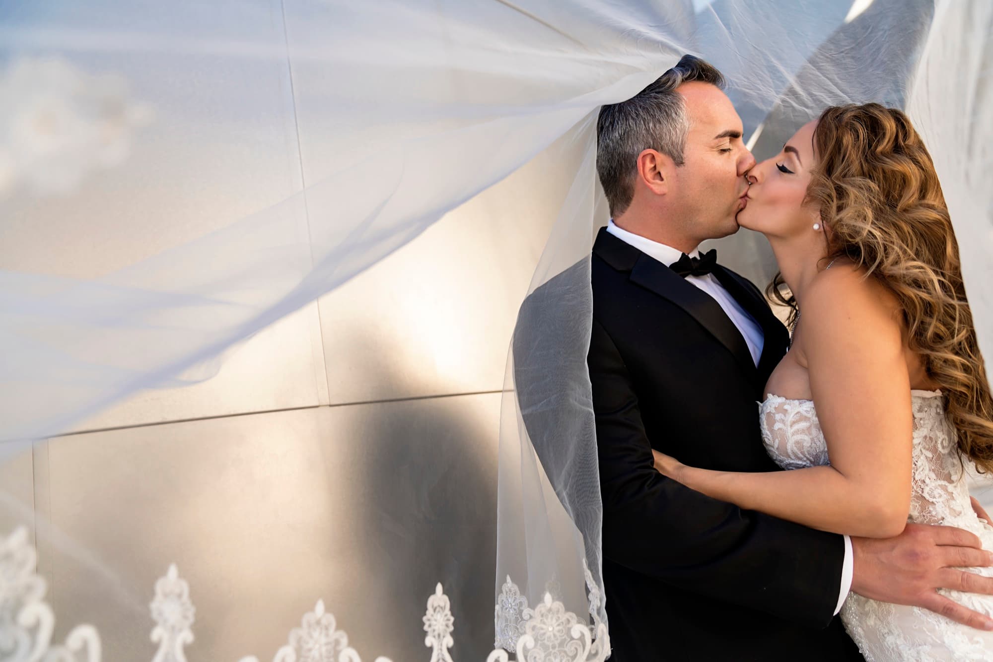 Suzie and Paul kissing beneath her cathedral veil against the bright steel wall of Walt Disney Concert Hall