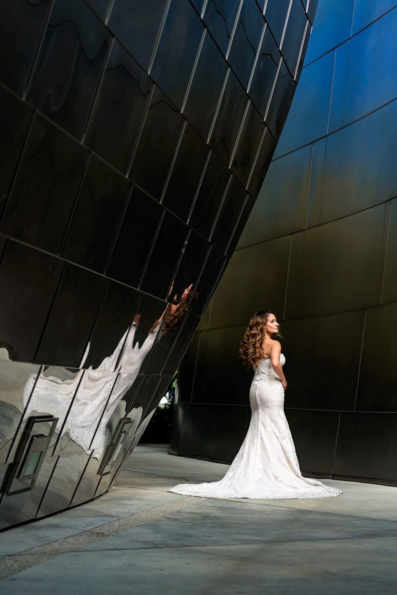 Suzie glowing in her gown against a dark curving steel wall of Walt Disney Concert Hall with her reflection beside her
