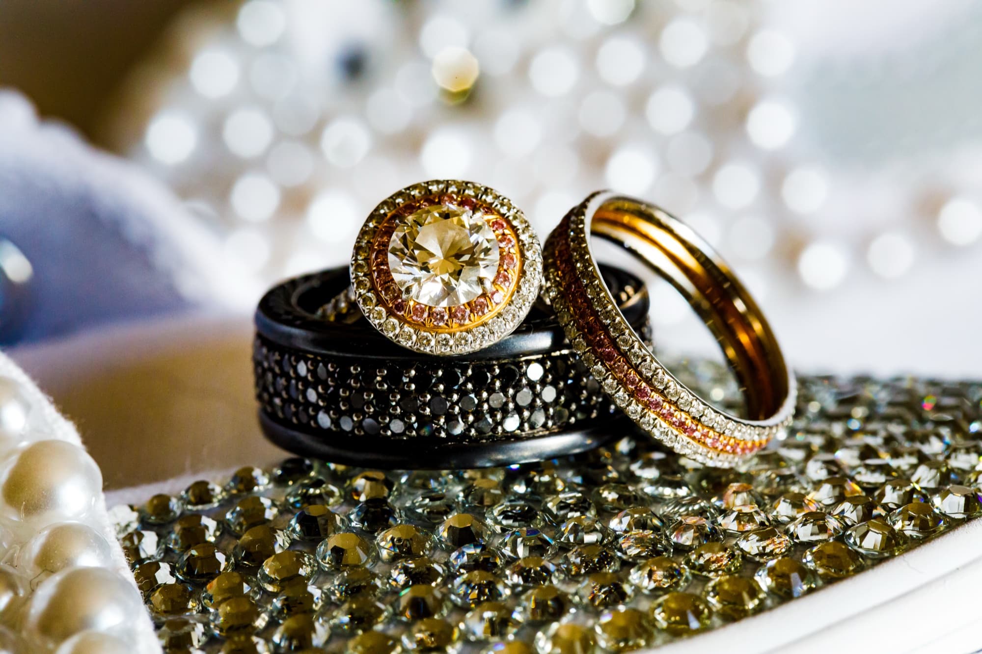 Champagne diamond engagement ring and black wedding bands photographed on pearl and crystal beadwork