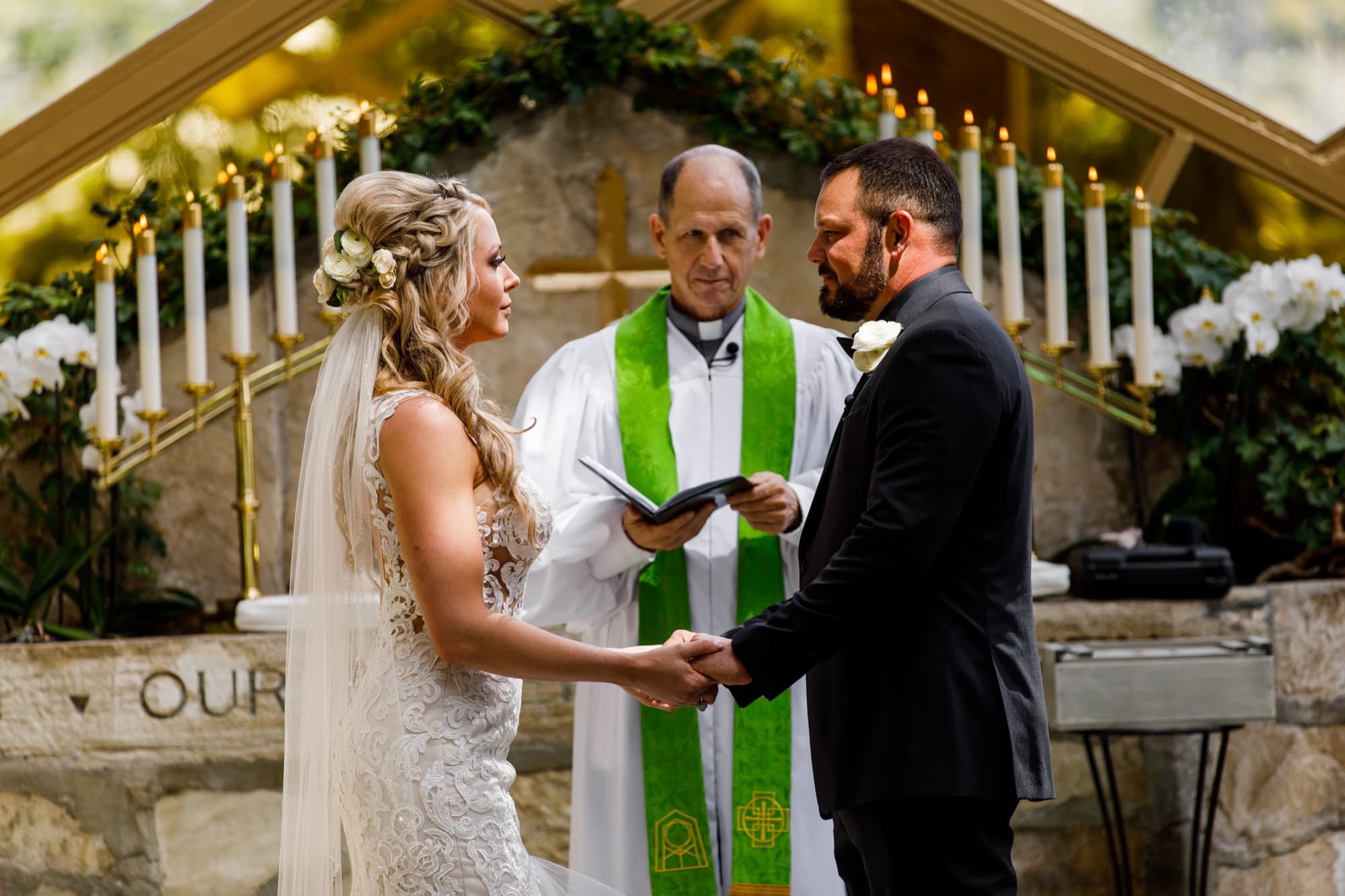 Amanda and Sean holding hands during their vows at the candlelit stone altar inside Wayfarers Chapel