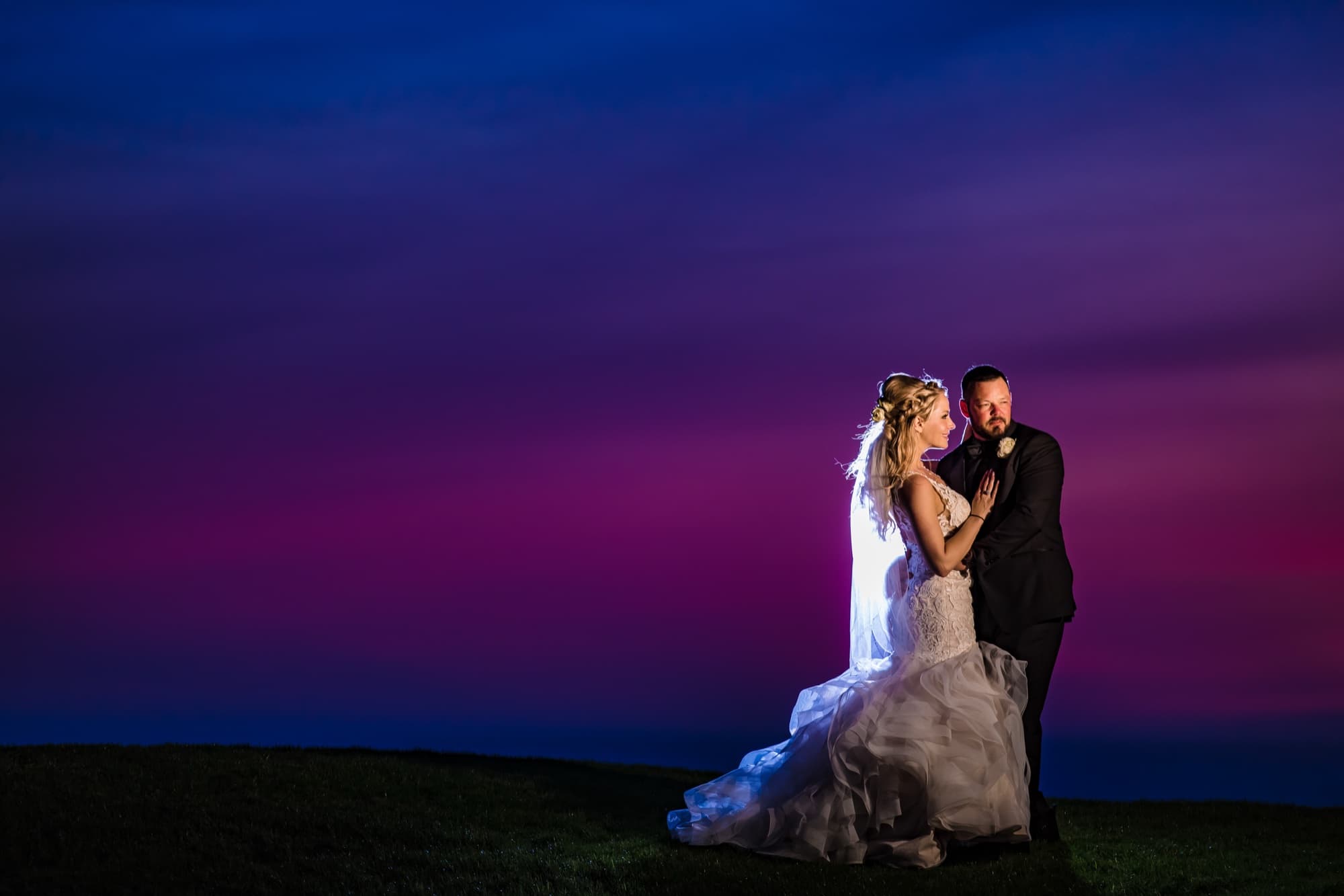 Amanda and Sean embracing on the dark lawn under a violet and magenta dusk sky at Trump National