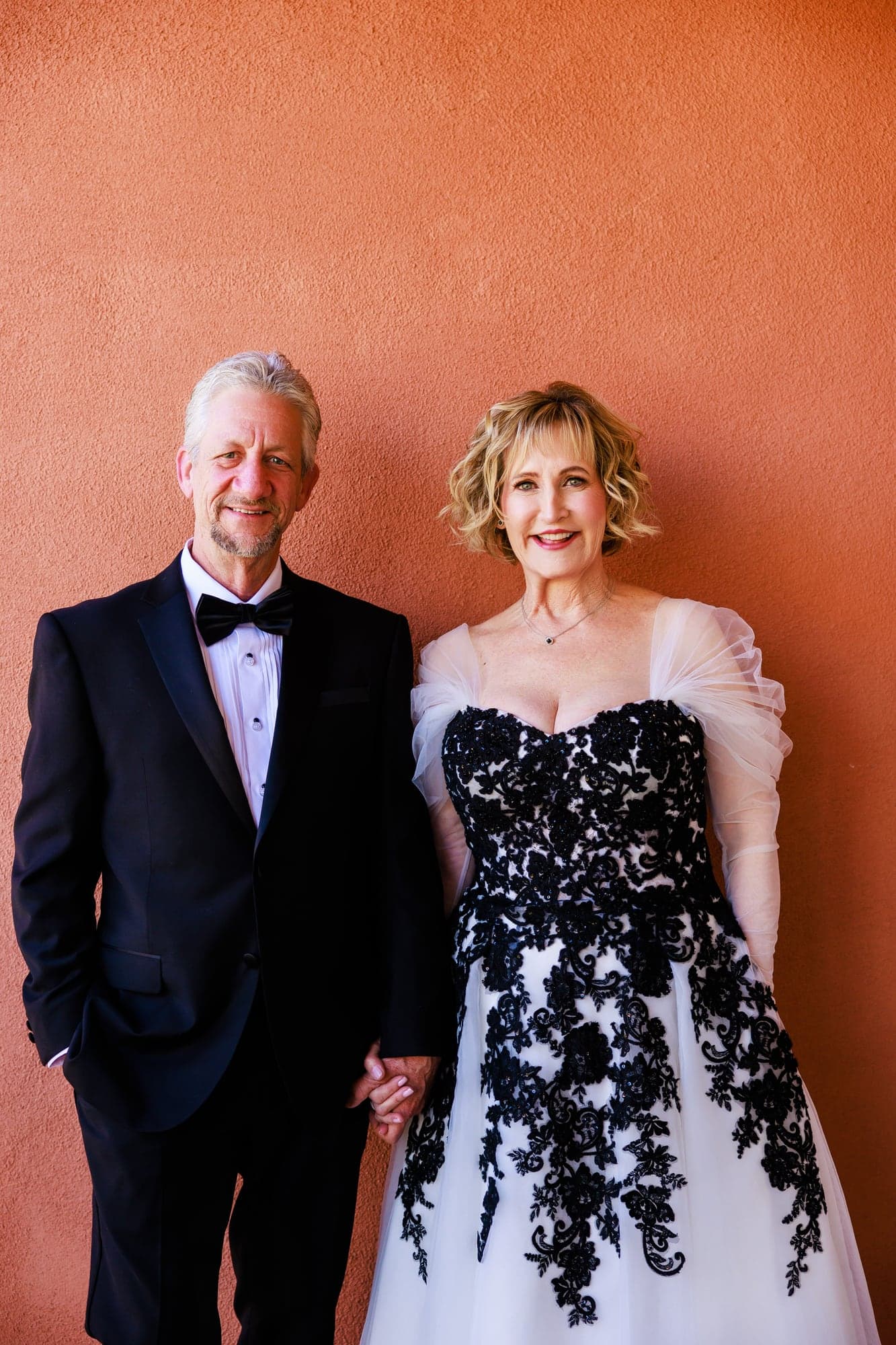 Donna and Greg in formal wedding attire against a warm textured wall