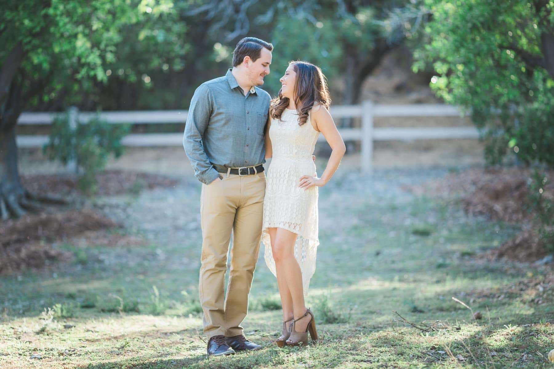 An engaged couple standing close together in a green field at dusk, a shallow depth-of-field portrait shot on the Canon 135mm f/2L