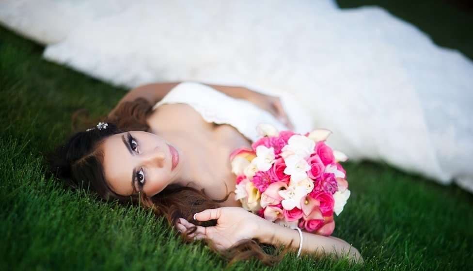 A bride lying in the grass holding a pink and white bouquet, a shallow depth-of-field bridal portrait shot wide open on the Canon 85mm f/1.2L