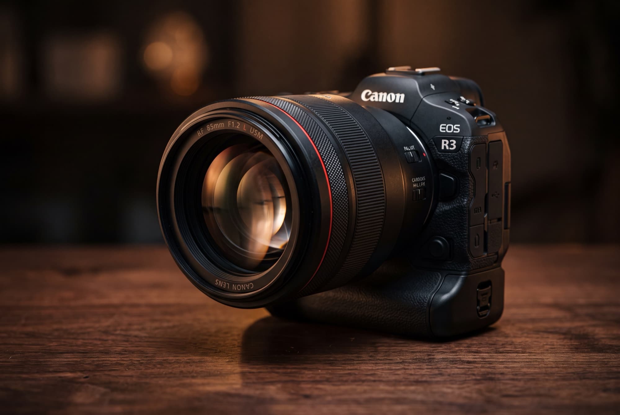 The Canon RF 85mm f/1.2L USM lens mounted on a Canon EOS R3 mirrorless body on a dark wood table, the native version the author shoots today