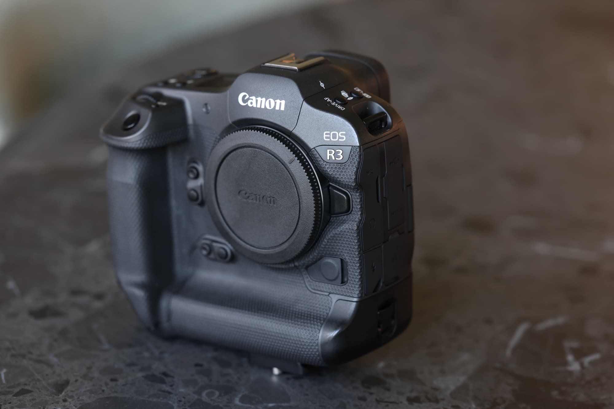 The author's own Canon EOS R3 body with its integrated vertical grip, photographed in window light on a dark marble counter