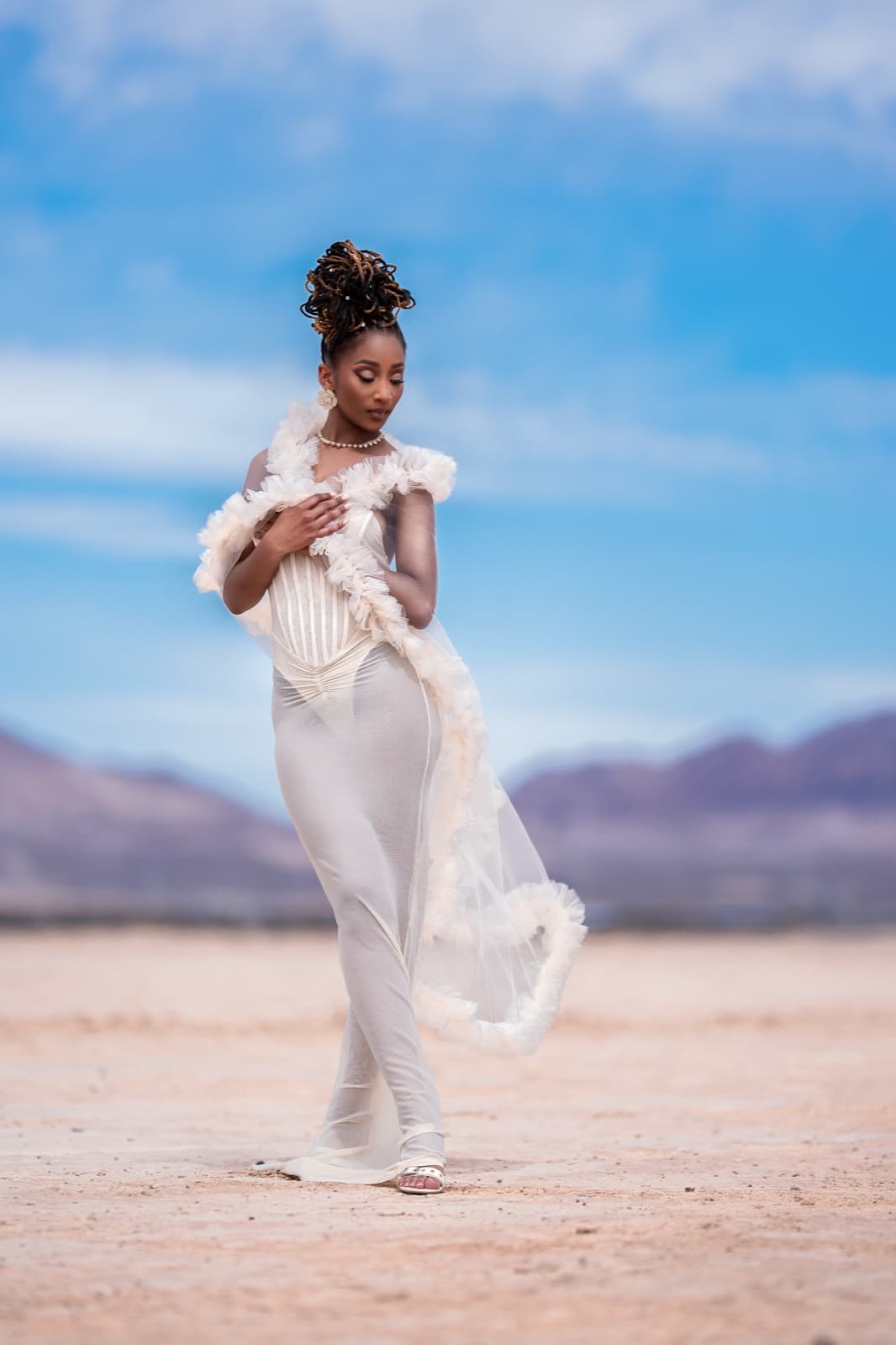 A woman in a white gown with ruffled details standing in a bright desert landscape under blue sky, photographed on Sony