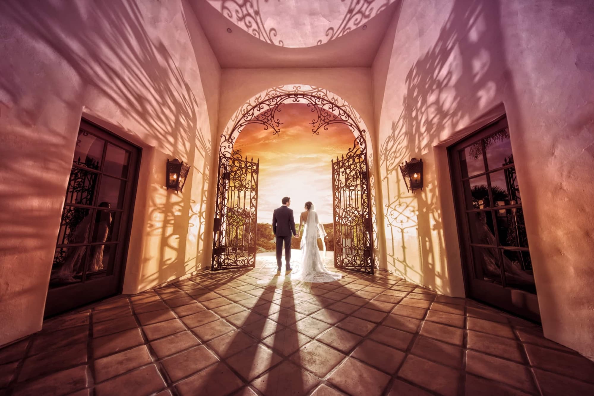 A couple standing in a sunlit Spanish-style archway corridor at Hummingbird Nest Ranch, silhouetted against a golden sunset