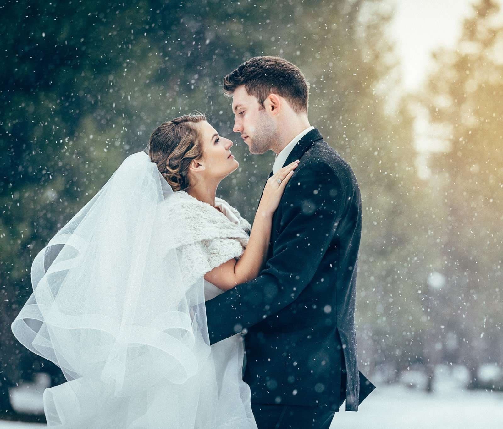 A bride and groom with foreheads together as snow falls around them at a winter destination wedding