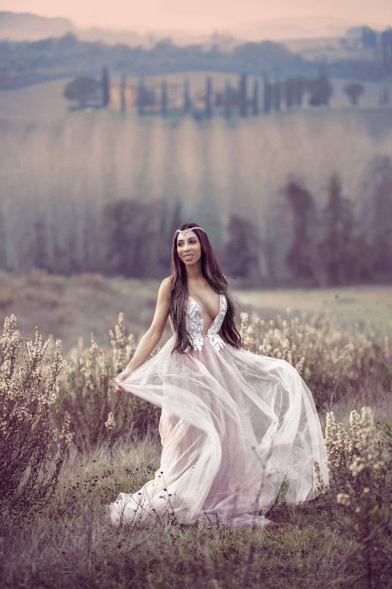 A bride kneeling in a golden Tuscan field at dusk in a flowing gown, photographed on the Canon EOS R in Italy