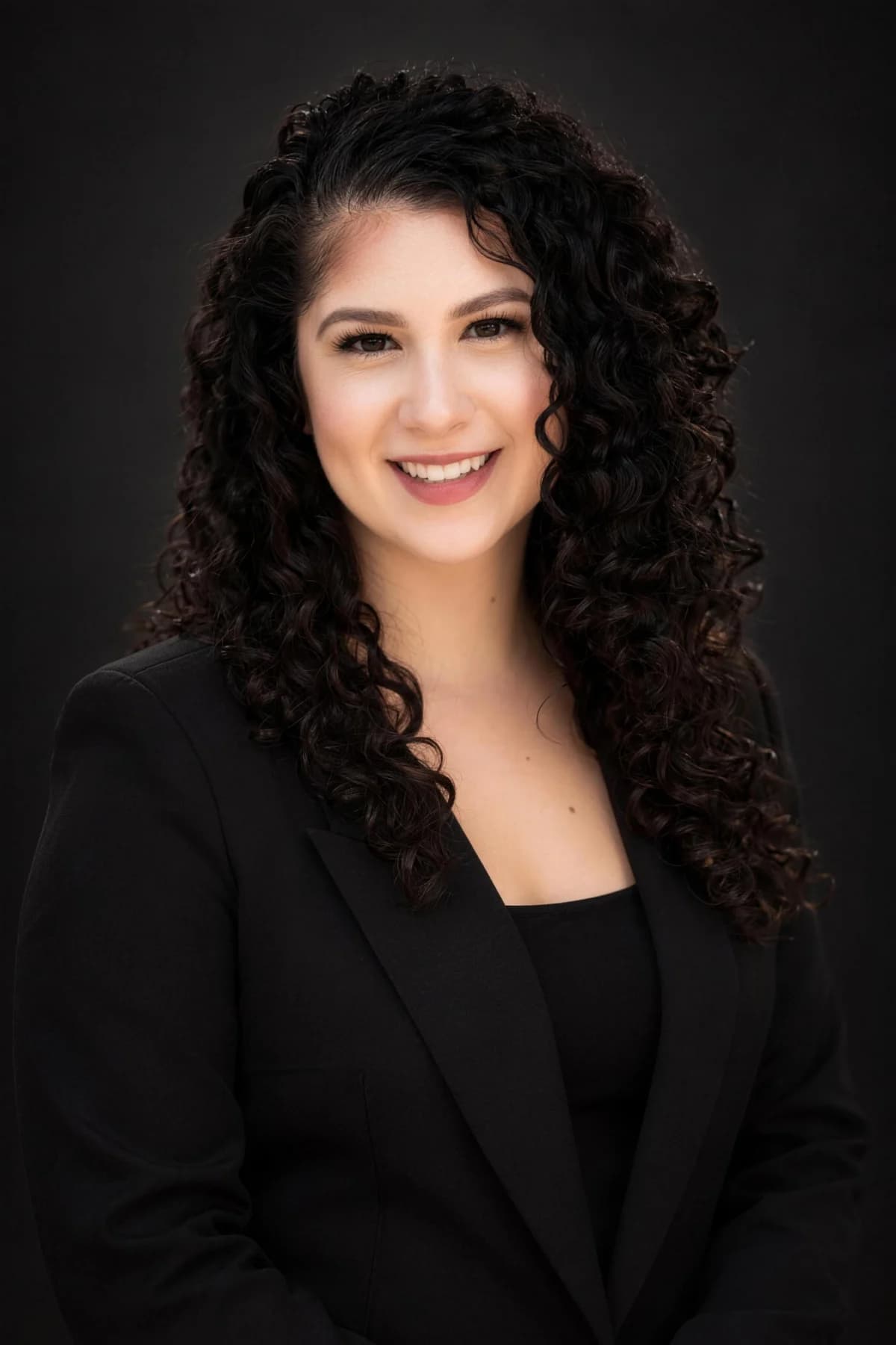 Courtney in a black blazer against a dark studio backdrop