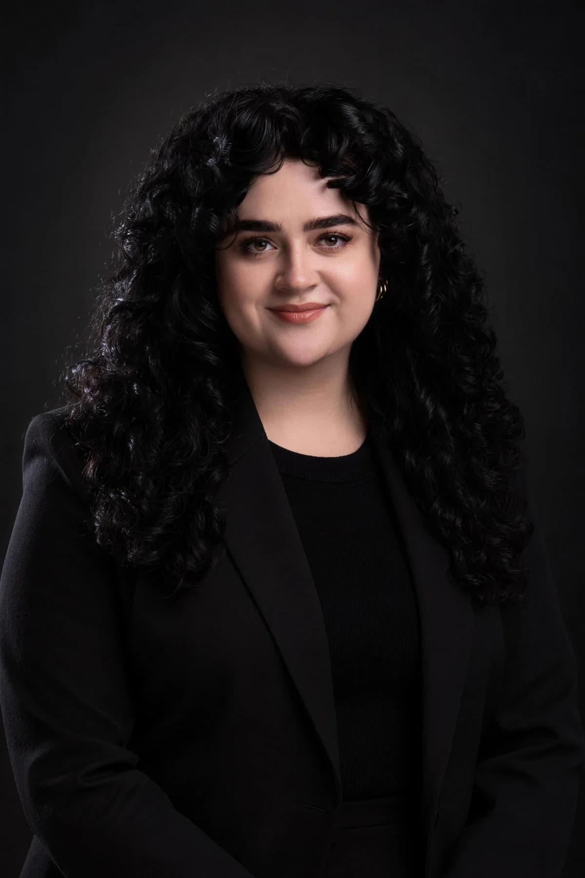 Juno in a black blazer against a dark studio backdrop